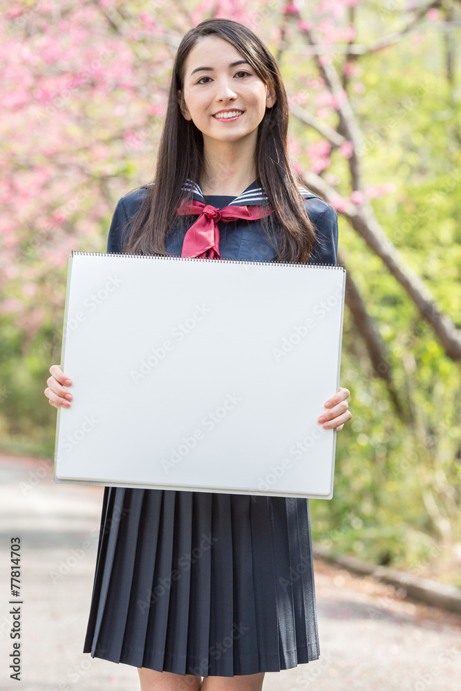 桜をバックにホワイトボードを持つ女子学生