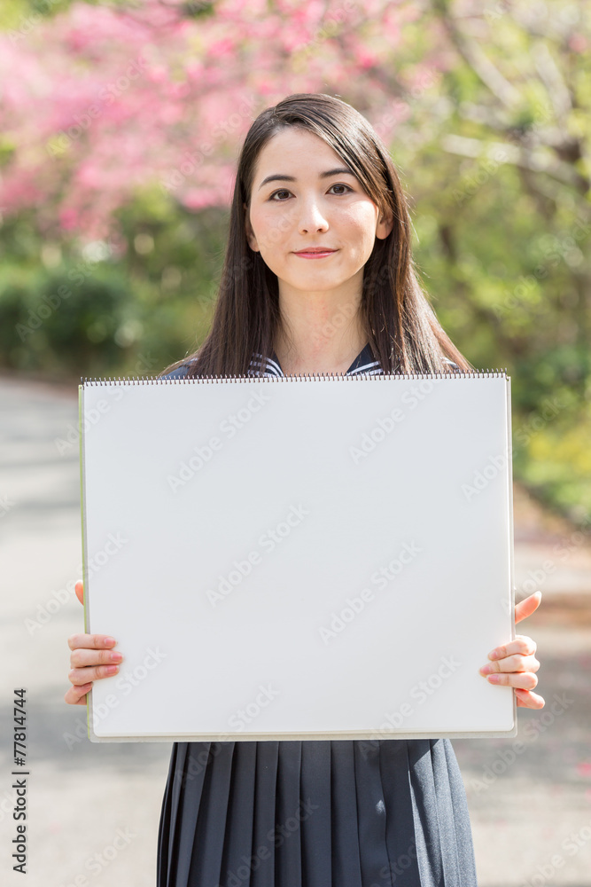 桜をバックにホワイトボードを持つ女子学生 桜をバックにホワイトボードを持つ女子学生