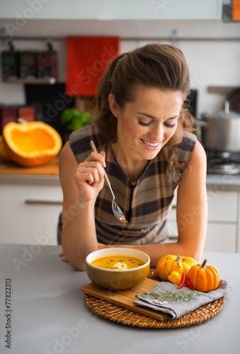Young housewife eating pumpkin soup in kitchen