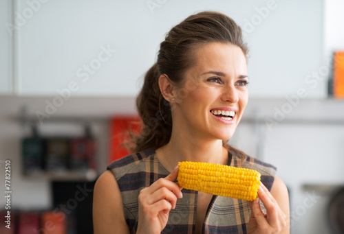 Portrait of happy young housewife eating boiled corn