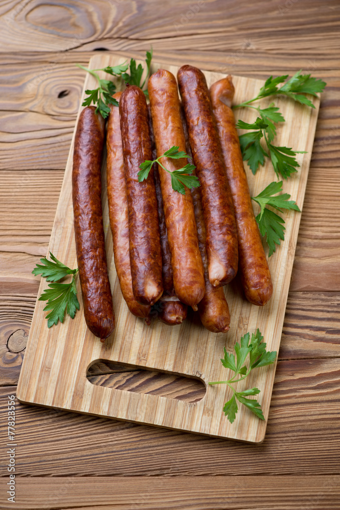 Wooden cutting board with sausages and parsley, high angle view