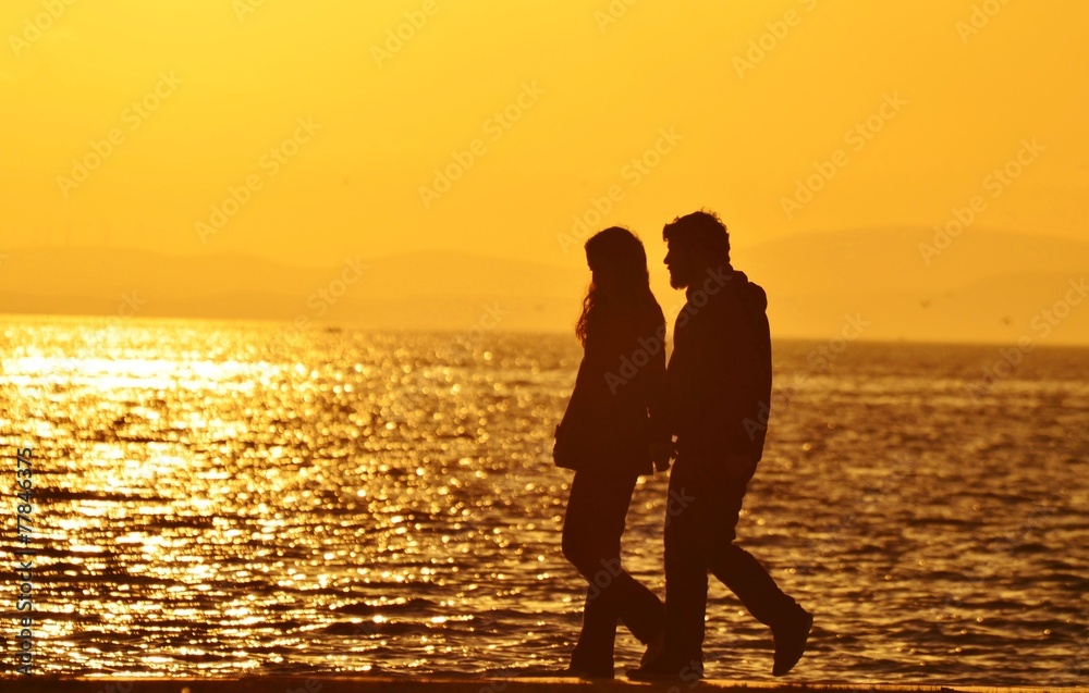 Young couple walking on beach under sunset