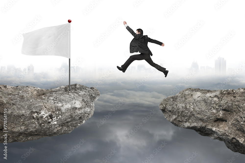 Businessman jump on cliff with white flag and cloudy cityscape Businessman jump on cliff with white flag and cloudy cityscape
