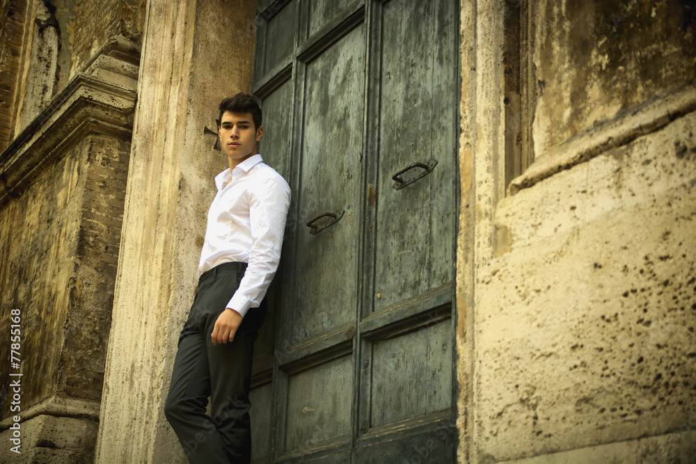 Elegant young man leaning against old wall and door