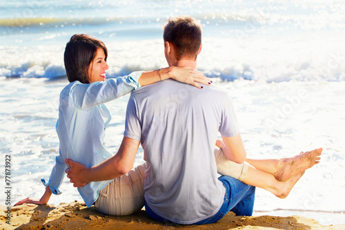 Couple Sitting on Sand at the Beach looking the sea