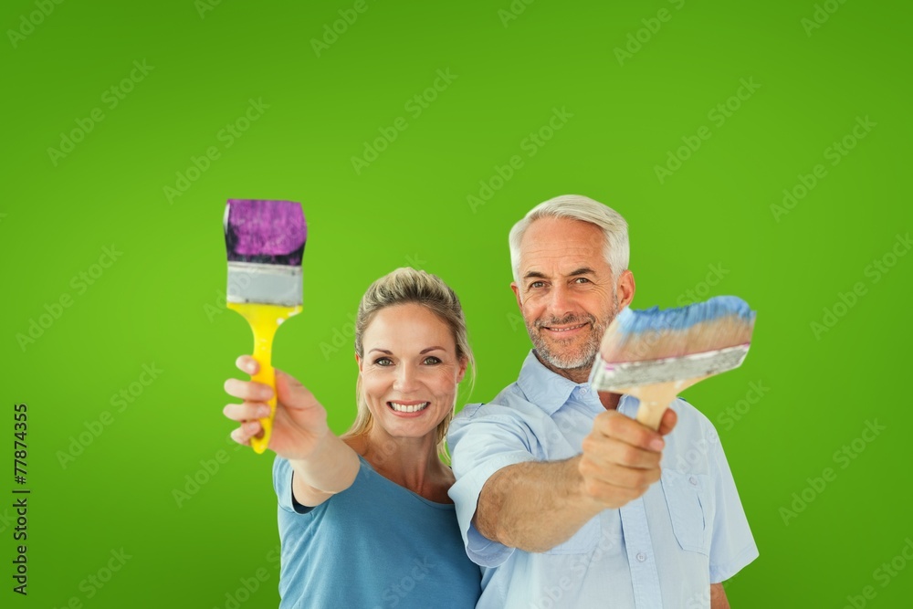 Happy couple holding paintbrushes smiling at camera Happy couple holding paintbrushes smiling at camera