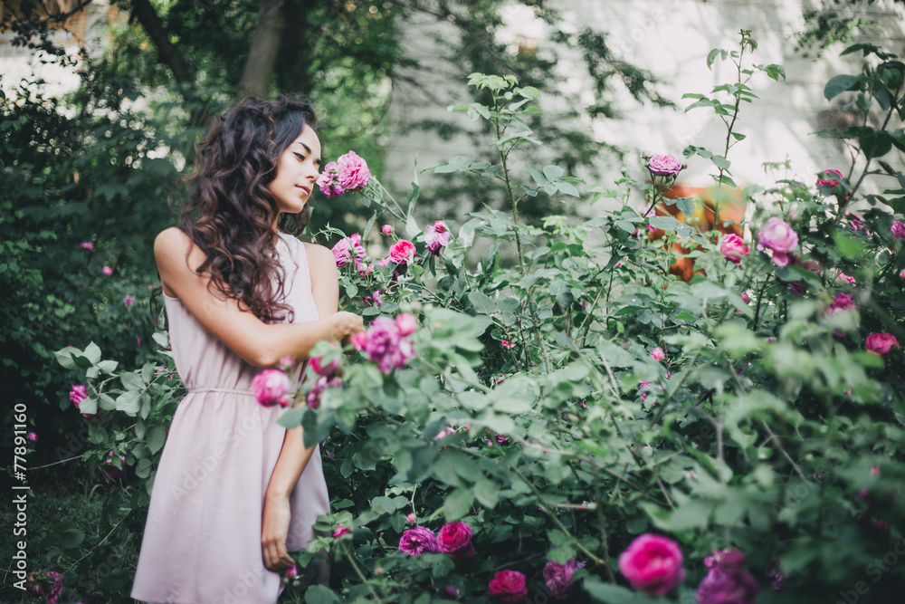 Beautiful young woman in a pink dress posing in a rose garden