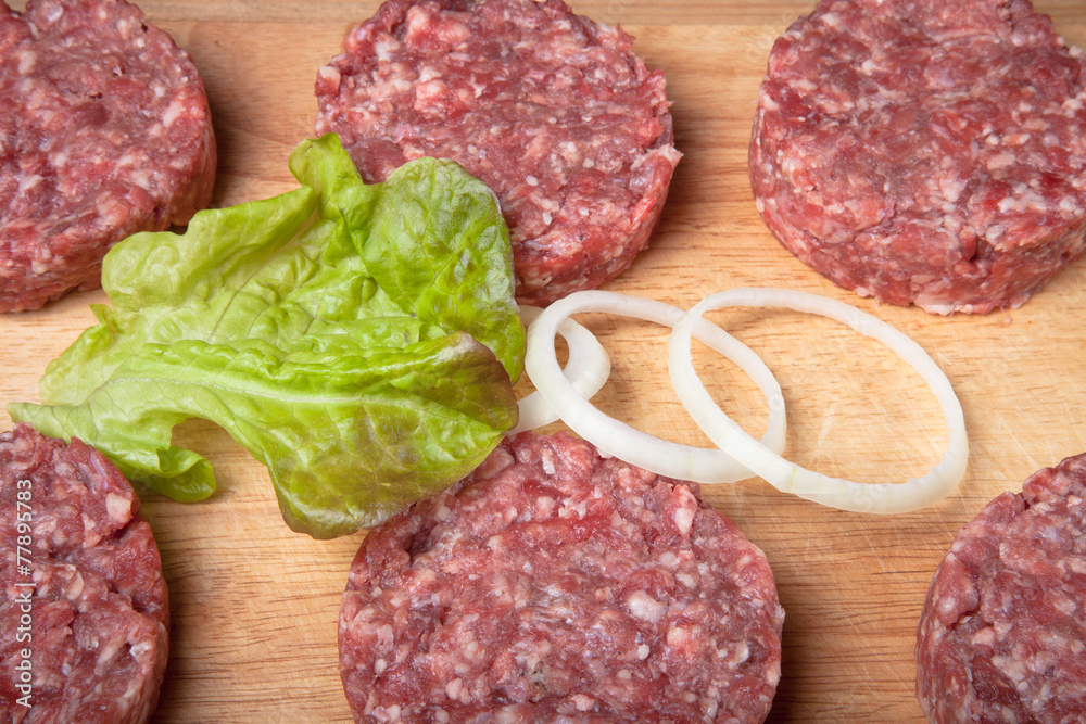 Raw cutlet of minced meat with leaf of salad and rings of onion Raw cutlet of minced meat with leaf of salad and rings of onion