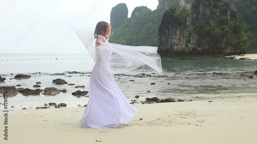 young blonde bride turns around barefoot with veil on sandy beac young blonde bride turns around barefoot with veil on sandy beac