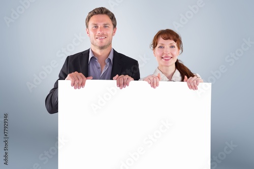 Composite image of smiling couple holding large sign