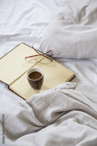 Kaffeetasse, Buch, Lesebrille auf Bett