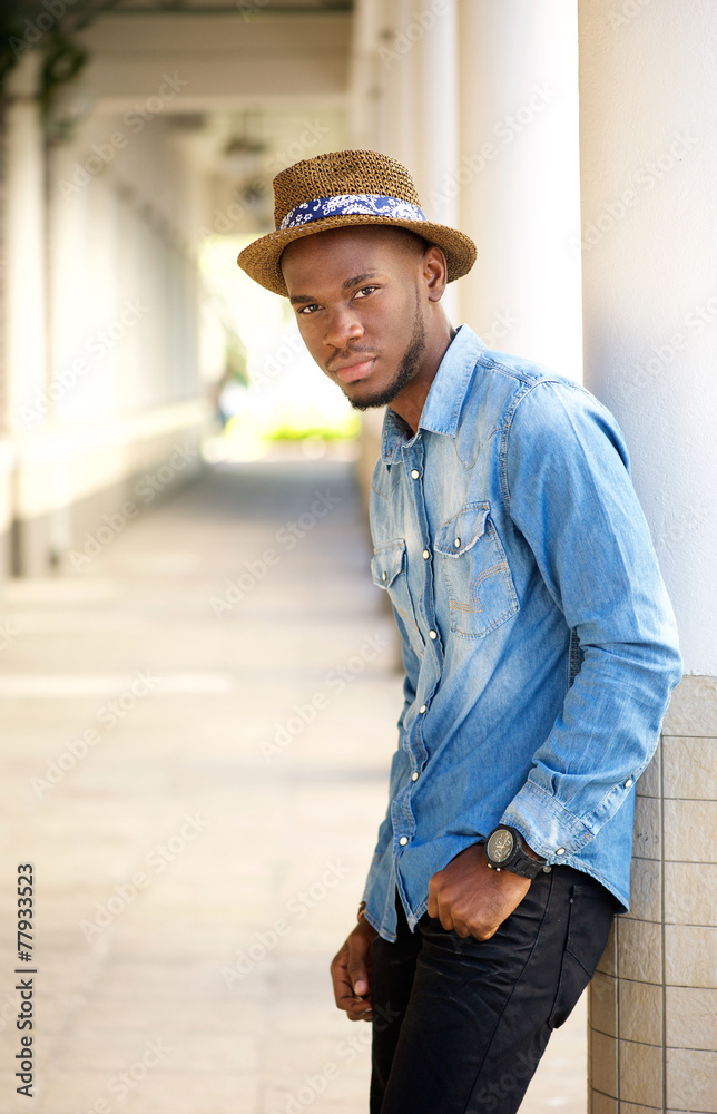 Relaxed young man with hat leaning on wall outdoors