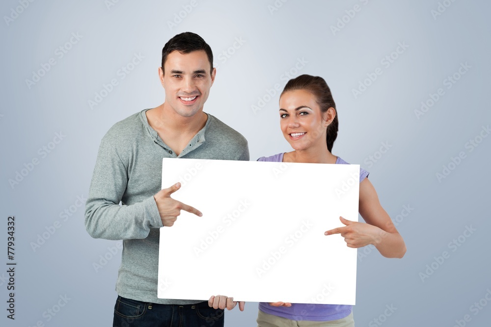 Smiling young couple pointing at sign they are holding Smiling young couple pointing at sign they are holding