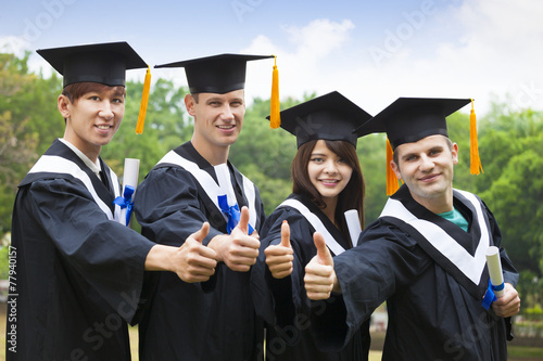 happy students in graduation gowns showing diplomas with thumbs