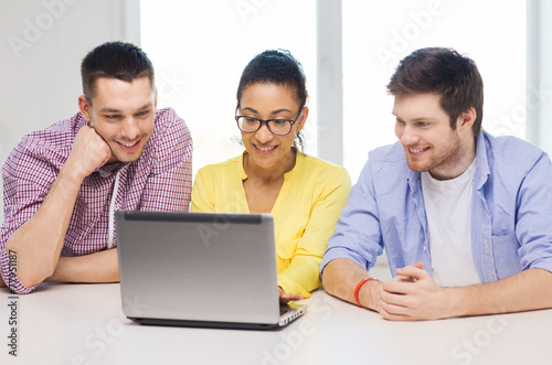 three smiling colleagues with laptop in office