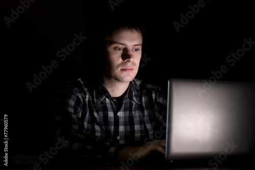Young man sitting at a laptop in the dark