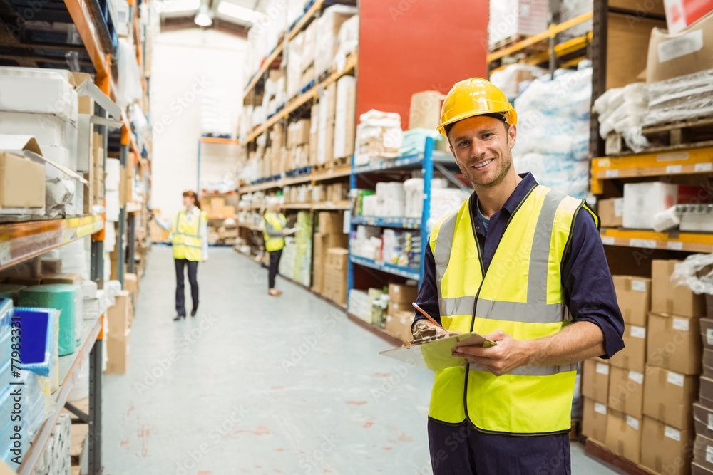 Warehouse worker smiling at camera with clipboard Warehouse worker smiling at camera with clipboard