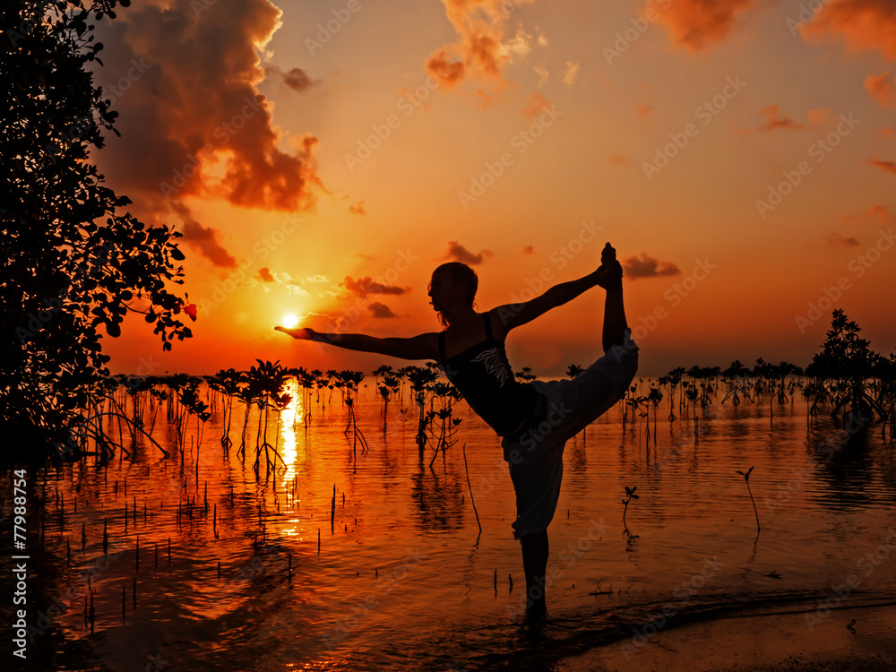 Young woman practicing yoga on the beach near mangroves