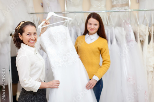 Woman helps the bride in choosing bridal gown