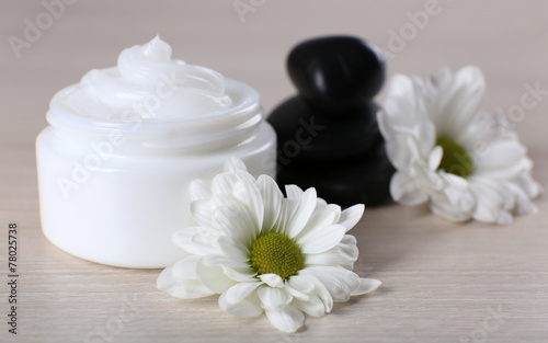 Cosmetic cream with spa stones and flowers on wooden background