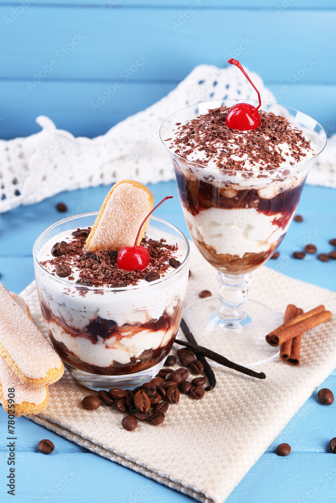 Tasty tiramisu dessert in glasses, on color wooden background Tasty tiramisu dessert in glasses, on color wooden background