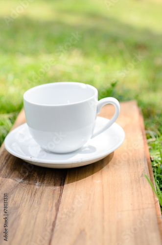 Blank coffee cup on wooden board with grass and natural light.