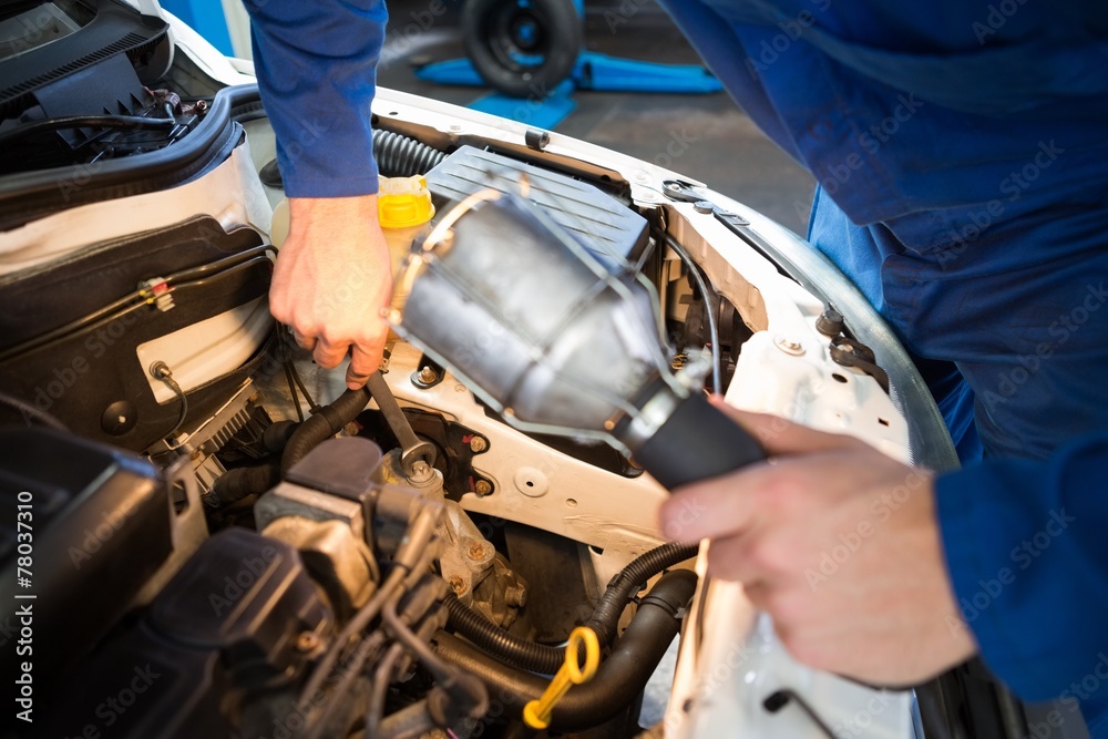 Mechanic examining under hood of car with torch Mechanic examining under hood of car with torch