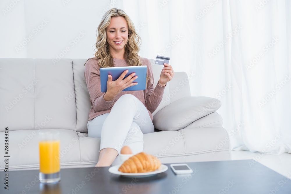 Smiling blonde sitting on couch shopping online Smiling blonde sitting on couch shopping online
