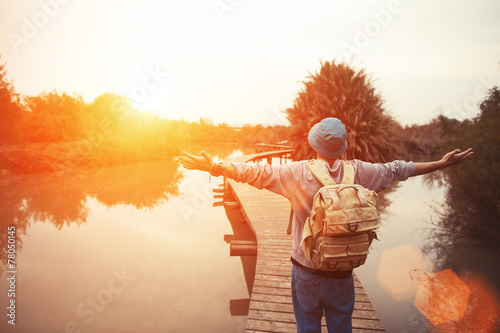 happy traveler on lake with outspread hands looking at sunset