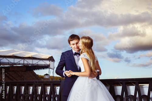 A newlywed couple is tenderly kissing against the sky view. photo