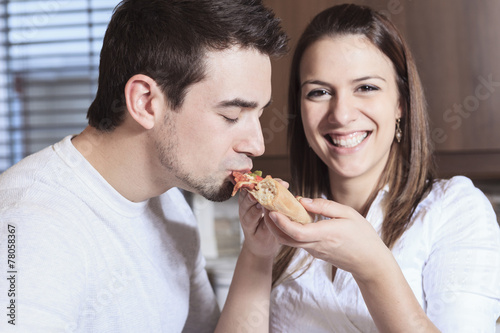 A Happy young couple eating pizza at the kitchen