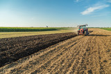 Farmer plowing stubble field with red tractor