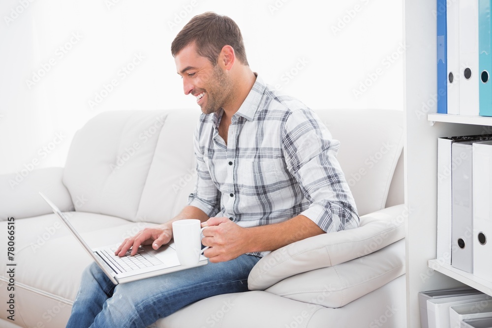 Smiling man with a mug using a laptop