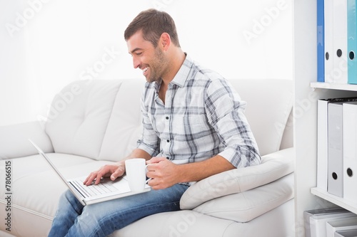 Smiling man with a mug using a laptop © WavebreakmediaMicro