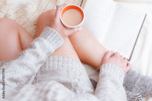 photo of a woman in a sweater with the old book and a cup of tea