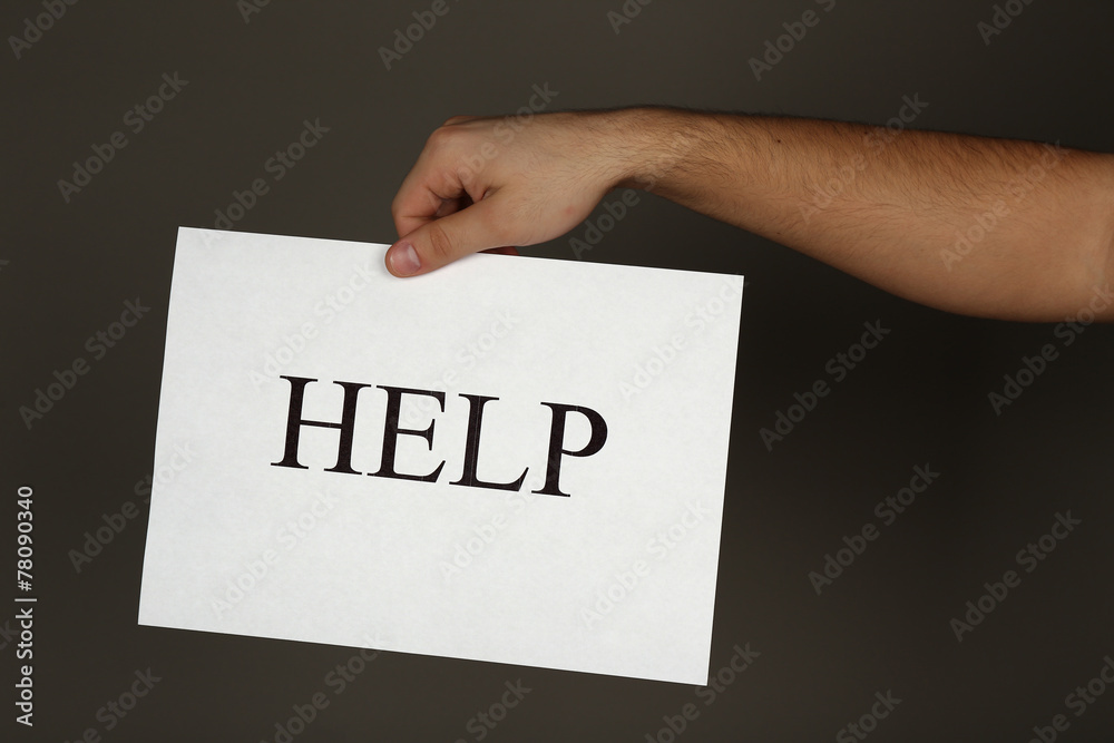 Sheet of paper with Help sign in male hand on dark background Sheet of paper with Help sign in male hand on dark background