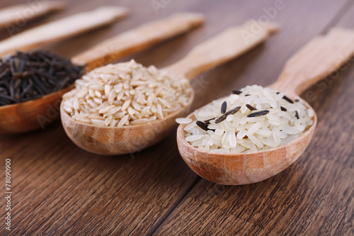 Different kinds of rice in spoons on wooden background