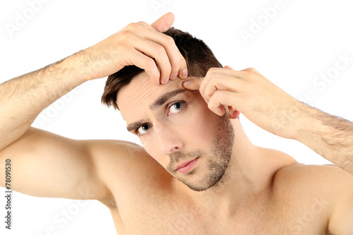 Handsome young man squeezing pimple isolated on white