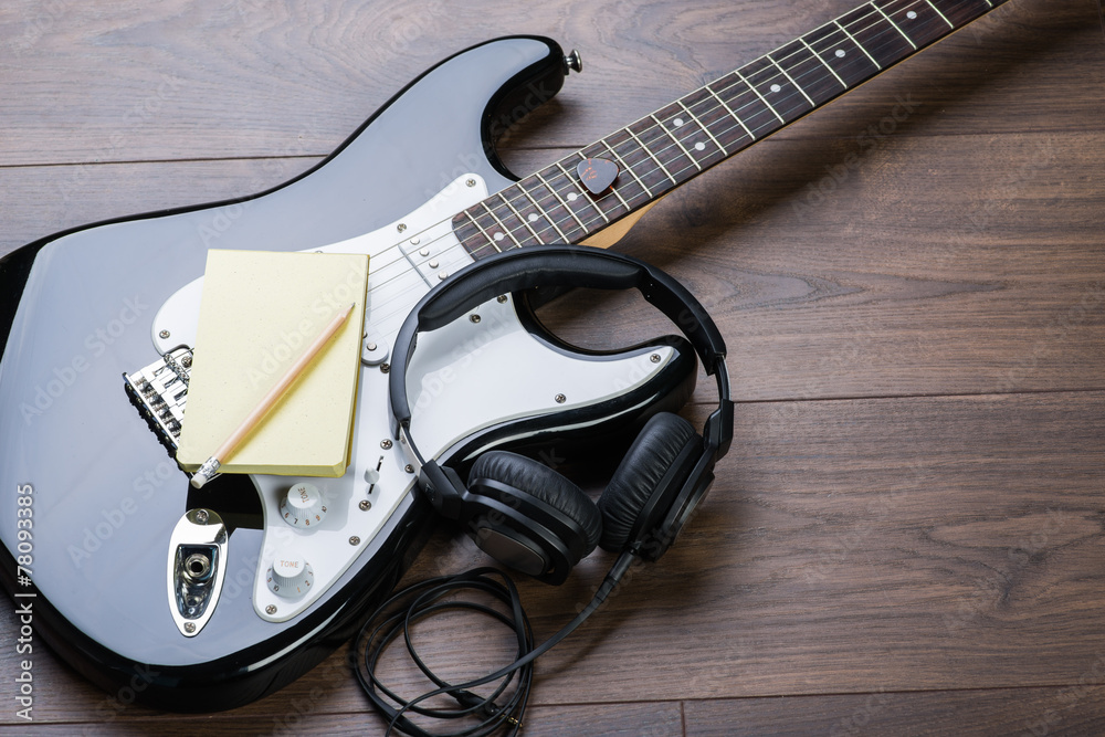 Naklejka premium Black electric guitar with notepad, headphones and pencil