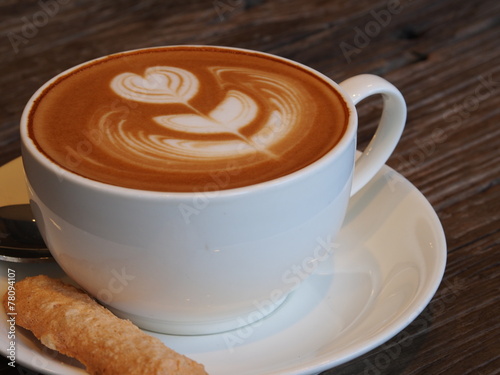 Latte art coffee and biscuit on the wooden desk. photo