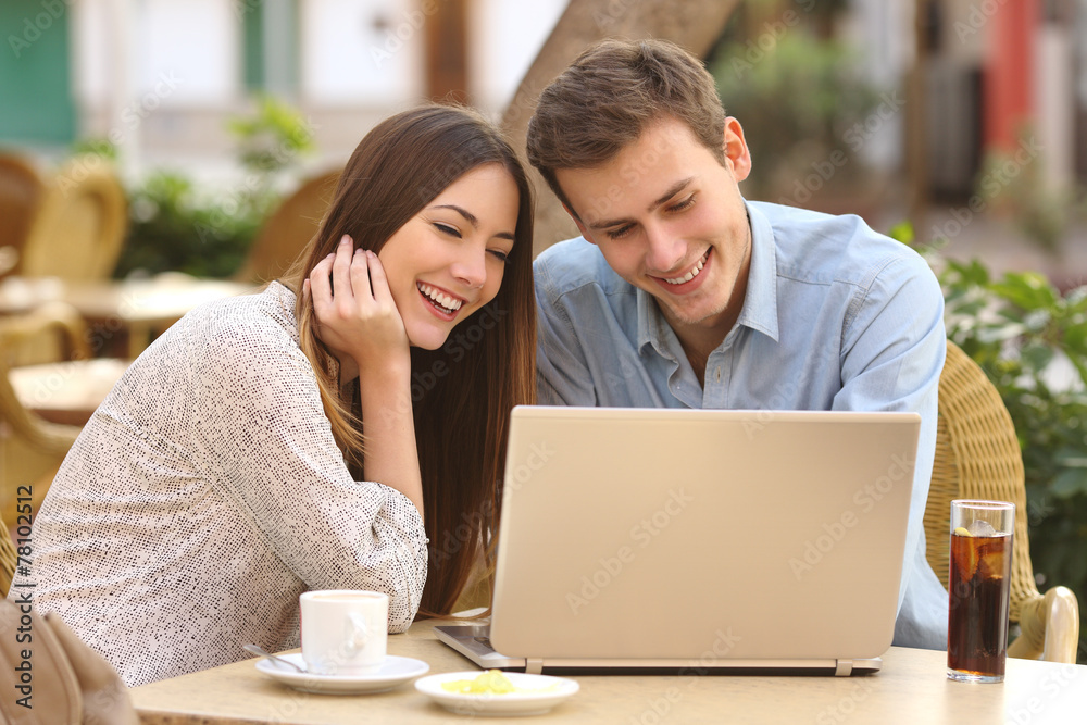 Couple watching media in a laptop in a restaurant Couple watching media in a laptop in a restaurant