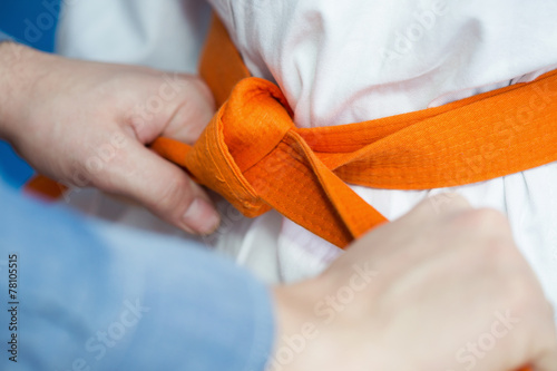 Father ties an orange belt on his son's martial arts uniform