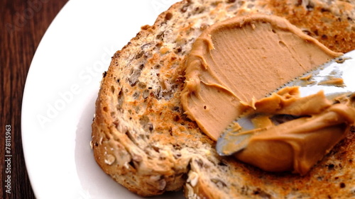 Peanut butter being spread on whole wheat toast