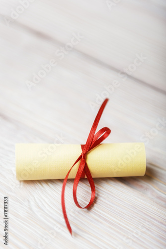 Rolled paper with red ribbon on white vintage wooden background