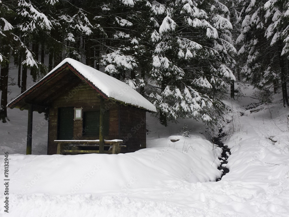 Holzhaus im Schnee neben Bach