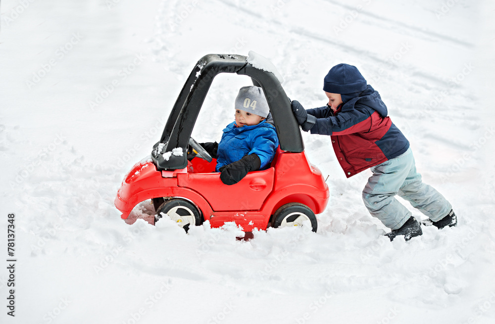 Fototapeta premium Young Boy Gives a Push to his Brother's Car Stuck in the Snow