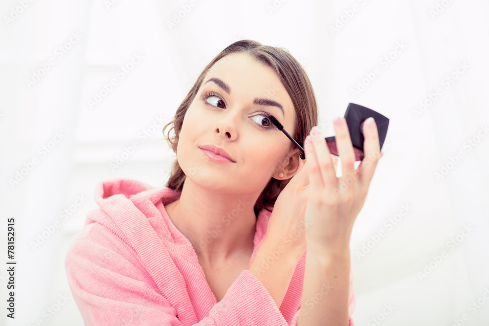 Beautiful young woman in bathrobe coloring her eyelashes Beautiful young woman in bathrobe coloring her eyelashes