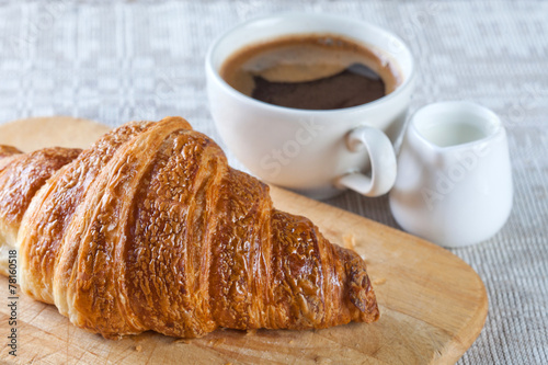 A cup of coffee with foam and croissant