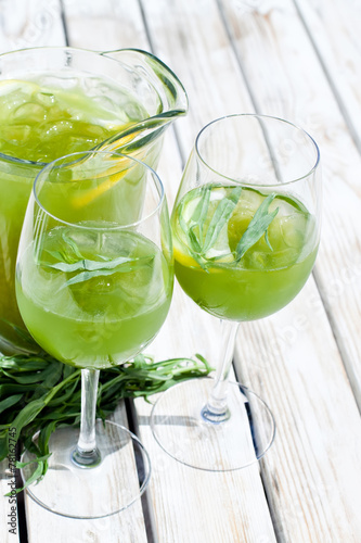 Green estragon lemonade pitcher with glasses on a wooden table