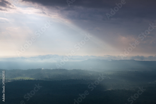 Sunlight shines through the clouds into the mountains and forest